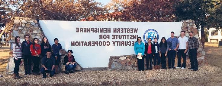 group of 14 people standing in front of the Western Hemisphere Institute for Security Cooperation sign